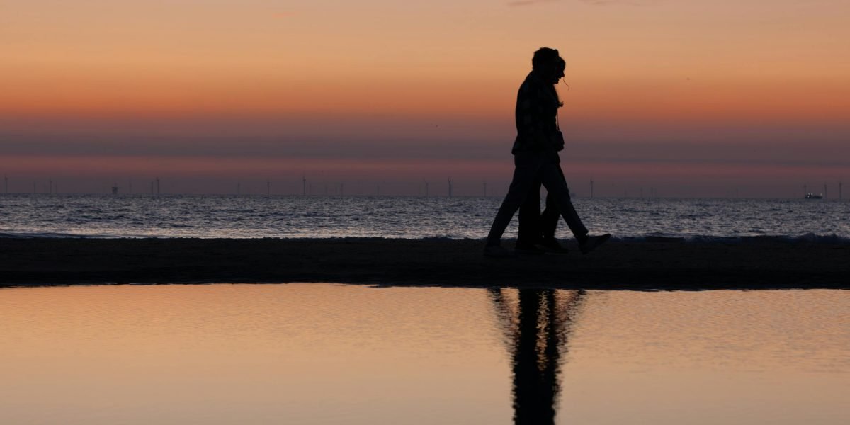 A couple enjoying a leisurely walk on a beach at sunset, embodying the serene and luxurious coastal lifestyle in Mina Seyahi.